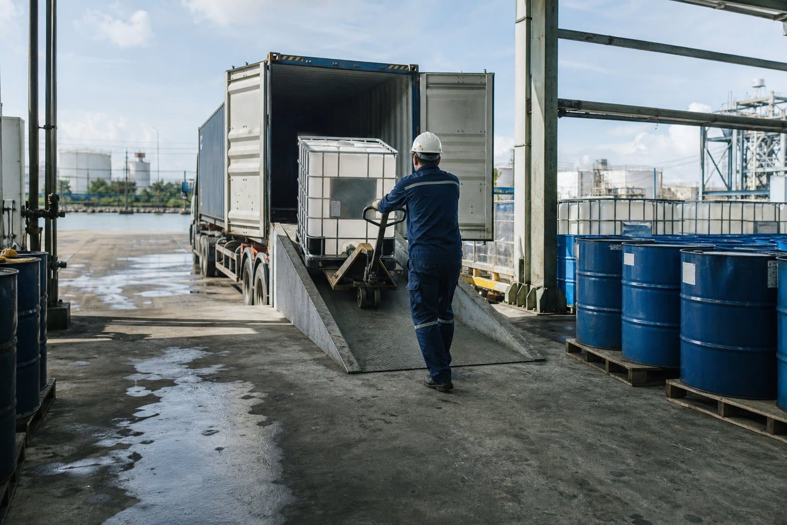 Công nhân hạ bồn IBC hóa chất từ container xuống bằng xe nâng tay tại kho gần cảng